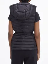 Chaleco negro acolchado con capucha, cierre frontal con cremallera, cinturón con hebilla metálica y bolsillos laterales con cremallera.