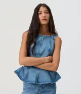 Blusa sin mangas confeccionada en jean de algodón, con escote redondo, corte entallado y diseño peplum con dobladillo evasé y recortes estructurados.