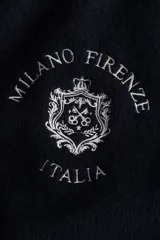 Campera de béisbol azul marino, ligeramente acolchada y confeccionada en tejido polar suave. Presenta cuello, puños y bajo acanalados con rayas blancas, hombros caídos, cierre frontal de botones a presión y bolsillos laterales ribeteados. Lleva un bordado en el pecho con texto que incluye "MILANO FIRENZE ITALIA".