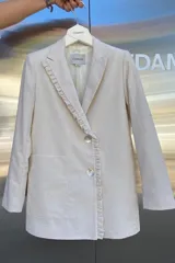 Blazer beige de lino con cuello con solapas, cierre frontal con botones de nácar, bolsillos amplios y volado en la solapa. Corte recto.