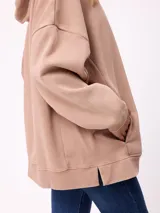 Canguro oversize de color gris con efecto lavado, capucha con cordones ajustables, bolsillo frontal tipo canguro y parche pequeño con logo de la marca en el pecho.