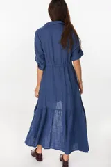 Vestido camisero largo de lino italiano color celeste, de corte relajado, con mangas caídas, jareta ajustable en la cintura, cierre frontal de botones y bajo con volado fruncido.