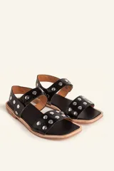 Sandalia baja de cuero vacuno color negro con acabado efecto charol texturizado, decorada con tachas metálicas plateadas en las tiras y la sujección del talón. Cuenta con suela plana de cuero.