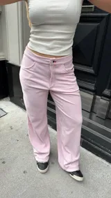 Pantalón de tiro medio confeccionado en tela jersey rib color rosa, con diseño de pierna ancha y bolsillos laterales. Presenta costuras visibles en hilo de color contrastante.