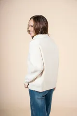 Cardigan de punto color crema, con cuello alto y cierre frontal parcial, de manga larga y diseño holgado.