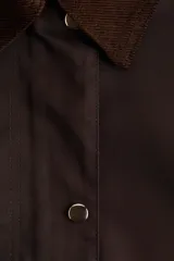 Campera de sarga color marrón oscuro, con cuello camisero de pana, cierre frontal oculto por solapa con botones a presión y bolsillos frontales grandes con solapa.