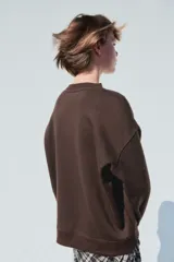 Buzo de corte oversized con cuello redondo, confeccionado en tejido con interior suave. Presenta hombros caídos, puños y bajo acanalados, y un diseño gráfico estampado en el pecho con estilo universitario.