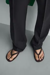 Sandalia tipo ojota o chancleta de goma, con base de color verde oscuro y tiras negras. Presenta una suela plana.