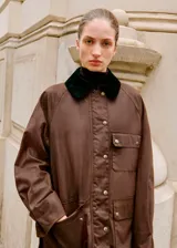 Parka de estilo encerado en color marrón, con diseño recto, cuello camisero de pana en contraste, cierre frontal con cremallera y botones, y múltiples bolsillos de parche con solapa.