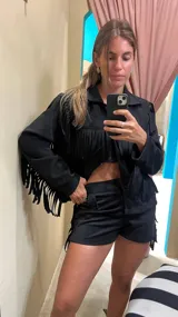 Campera negra con flecos en el pecho y en los hombros, con cuello camisero, cierre frontal con botones a presión y bolsillos de parche.