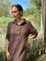 Vestido camisero largo de lino blanco, con cuello camisero, manga corta enrollada y cierre frontal de botones de nácar. Presenta aberturas laterales en el bajo.