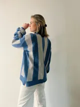 Sweater de punto con diseño de rayas verticales en tonos azul y gris, con sutil acabado brillante. Presenta cuello redondo, mangas largas con puños ajustados y corte amplio con aberturas laterales en el ruedo.