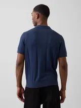 Buzo tipo polo color blanco óptico, de manga corta, tejido de punto con detalles de calados verticales en el frente y pequeño bordado alusivo en el pecho.