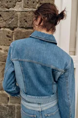 Cazadora corta de denim con cuello solapa y manga larga. Presenta un diseño de lavado combinado a contraste, con bolsillos de plastrón con solapa en el pecho y cierre frontal con botones metálicos.
