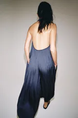 Mono largo satinado de color azul marino, con cuello halter, escote en V profundo y espalda descubierta. Presenta diseño plisado y bajo abullonado con terminación en puño.