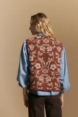 Chaleco tejido de punto con diseño floral ornamental, de silueta recta y cierre frontal con botones. Presenta una estética romántica y sofisticada, ideal para superponer sobre otras prendas.