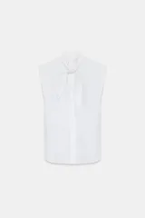 Camisa sin mangas de algodón con cuello redondo y detalle de lazada frontal. Presenta un diseño de corte recto con bajo redondeado y cierre frontal mediante botones ocultos bajo una solapa.