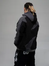 Campera con capucha confeccionada en tejido tipo polar, con diseño de bloques de color en tonos negro y gris oscuro. Presenta cierre frontal completo y ajuste regular.