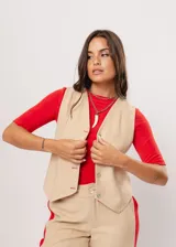 Chaleco beige con escote en V, sin mangas y cierre frontal con botones. Presenta pespuntes en color rojo y logo bordado en la espalda.