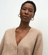 Cardigan de punto color beige con escote en V, cierre frontal con botones grandes y mangas largas con puños acanalados. Presenta un corte recto y estructurado.