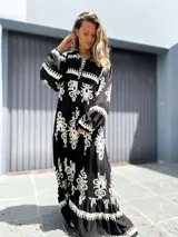 Vestido largo estilo túnica, color negro con estampado ornamental en blanco. Presenta cuello en V con botones y mangas largas amplias.