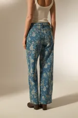 Pantalon de jean de corte recto con estampado floral en tonos claros sobre base azul. Presenta bolsillos funcionales y tiro medio.