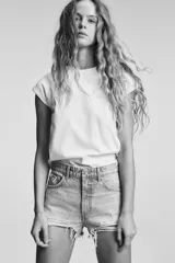 Short de jean negro desgastado, tiro alto, con roturas pronunciadas y terminación deshilachada en el bajo. Presenta cinco bolsillos y cierre frontal con botón metálico.