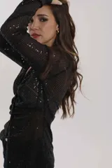 Camisa negra traslúcida con brillos, cuello clásico, cierre frontal con botones y mangas largas con puños abotonados.