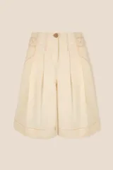 Bermuda de tiro alto en color crudo, confeccionada en lona de algodón. Presenta un corte acampanado con pliegues en la cintura, bolsillos delanteros inclinados y costuras decorativas en contraste color camel.