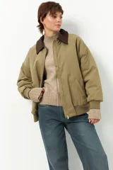 Campera estilo bomber color verde oliva, con cuello de pana marrón oscuro, cierre frontal y puños y cintura de elástico acanalado.