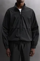 Chaqueta negra regular fit, confeccionada en tejido técnico con algodón. Presenta cuello subido, manga larga, forro interior de red y abertura en la espalda para transpiración. Incluye bolsillos con cierre de cremallera en la cadera, acabados elásticos y cierre frontal con cremallera.