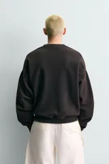 Sudadera de corte relajado color negro con efecto lavado, cuello redondo, manga larga y puños en rib. Presenta un estampado gráfico a contraste en el pecho con el texto 'General Service Goods'.