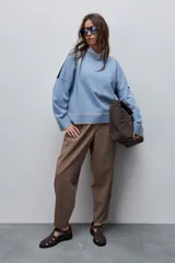 Sweater tejido celeste de calce relajado con cuello redondo, hombros caídos y puños y ruedo acanalados con detalles en tono tostado.