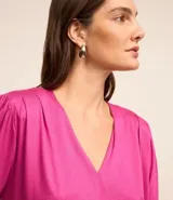 Blusa fucsia de viscolycra crepada, con escote en V y mangas cortas con detalle de pliegues en los hombros.