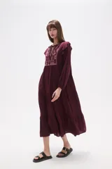 Vestido midi holgado de viscosa color vino tinto, con mangas largas y volados en los hombros. Presenta un canesú con bordado floral en tonos rosados y cuello con abertura en forma de lágrima y lazo para atar.
