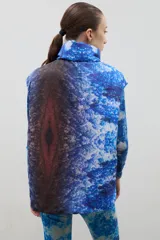 Chaleco puffer con cuello alto y cierre frontal oculto, con estampado forestal en tonos azules.