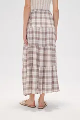Falda larga de algodón con diseño a cuadros en tonos beige, blanco, marrón y celeste. Presenta un diseño escalonado con volados y una abertura lateral pronunciada.