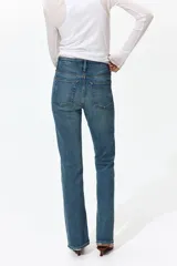 Jean de tiro alto y corte bootcut, confeccionado en denim de algodón levemente elástico con lavado azul medio y efecto desgastado. Presenta diseño clásico de cinco bolsillos, cierre de cremallera y botón metálico.