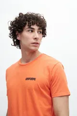 Remera naranja de algodón con cuello redondo y manga corta. Estampa pequeña con la palabra "UNIFORM" en el frente.