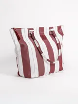 Bolso tipo tote grande, resistente al agua, con diseño de rayas verticales rojas y blancas. Cuenta con asas largas de hombro, cierre superior y parche de cuero con logo grabado. Incluye neceser transparente a juego con base y detalles a rayas.