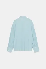 Camisa de rayas finas color amarillo, confeccionada con cuello redondo y lazada en el mismo tejido en el escote. Presenta mangas largas con hombros caídos y puños anchos abotonados.