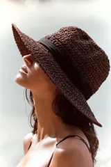 Sombrero de ala ancha color marrón tejido en paja, con cinta negra contrastante alrededor de la copa.