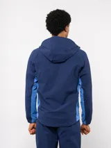 Campera deportiva Umbro del Club Nacional de Football, modelo Summit. Presenta un diseño con bloques de color en azul, rojo y blanco, con capucha, cierre frontal y bolsillos laterales con cierre. Incluye el logo de la marca y el escudo del club en el pecho.