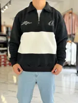 Buzo de algodón negro con una franja horizontal blanca en el centro, cuello solapa con medio cierre y puños y cintura elásticos acanalados. Cuenta con pequeños estampados en el pecho.