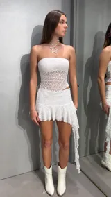 Minifalda de encaje blanco con short incorporado, tiro bajo, diseño asimétrico con volados y un lateral más largo que cae en punta.