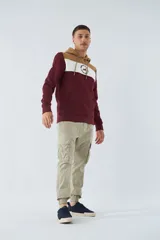 Buzo canguro de felpa color borgoña, con capucha ajustable con cordones color beige, bolsillo tipo canguro y logo estampado en el pecho. Tiene una franja horizontal blanca en el pecho y puños y cintura acanalados.