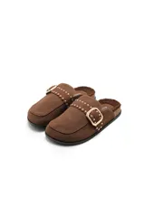 Pantuflas de gamuza color marrón con interior de corderito sintético. Presentan una banda decorativa con tachas metálicas y una hebilla dorada ajustable sobre el empeine, con suela de goma.