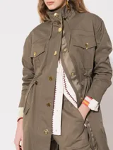 Parka verde militar de gabardina con mangas largas, jareta en cintura, ruedo y cuello con cordón interno al tono. Acceso frontal con broches dorados. Bolsillos delanteros y laterales.