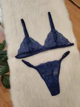 Conjunto de lencería de encaje en color azul profundo, compuesto por un corpiño triangular sin aro y una bombacha tipo colaless con detalles de encaje y transparencias.