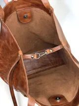 Bolso tipo tote grande de cuero genuino marrón, con asas de hombro dobles, bolsillo exterior con botón a presión y llavero colgante con la marca grabada.